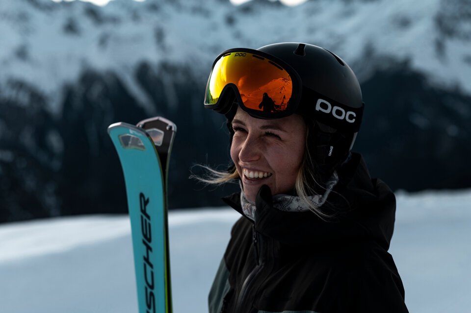 © Fischer Sports GmbH Woman smiling in ski gear with mountains in the background. | © Fischer Sports GmbH