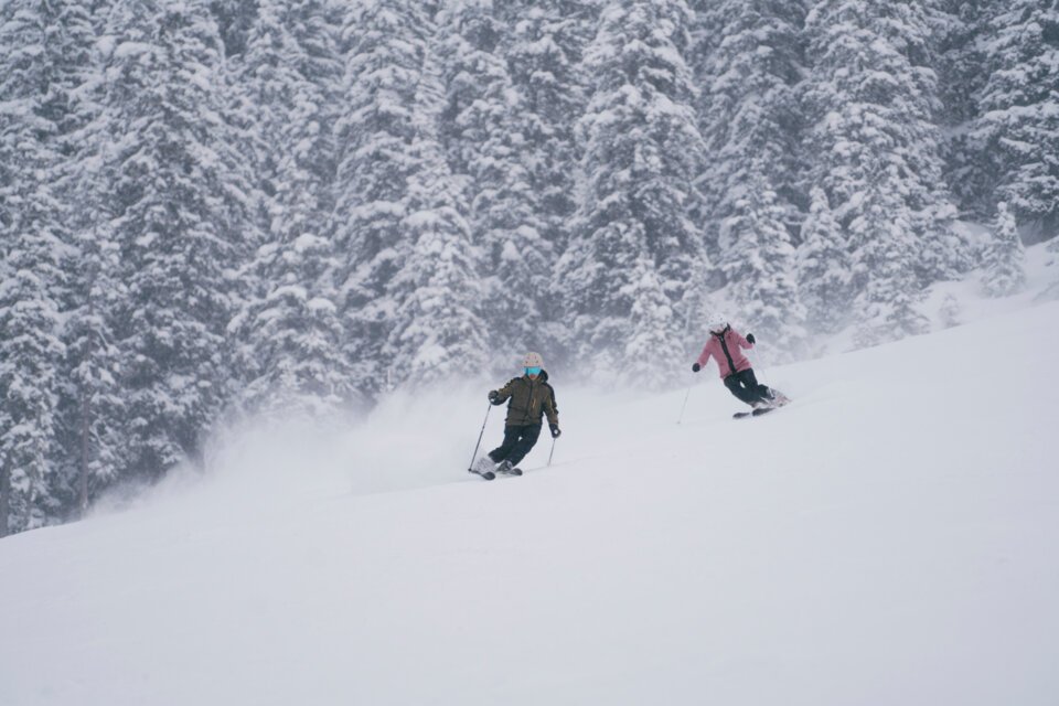 © INTERSPORT International Corporation GmbH Two skiers on a snowy slope with a forested backdrop. | © INTERSPORT International Corporation GmbH