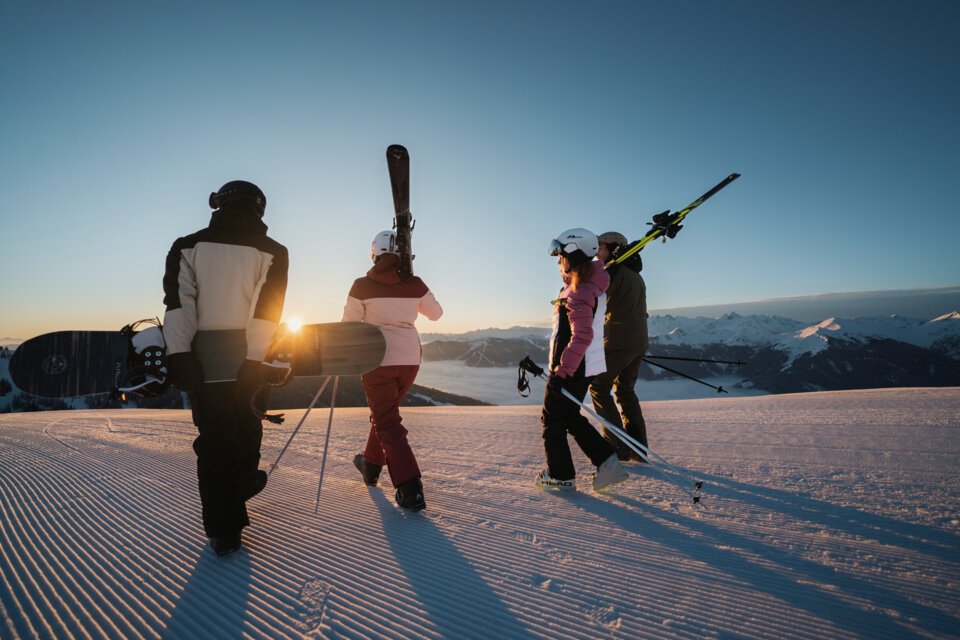 © INTERSPORT International Corporation GmbH Group of skiers and snowboarders walking at sunset on a groomed slope. | © INTERSPORT International Corporation GmbH