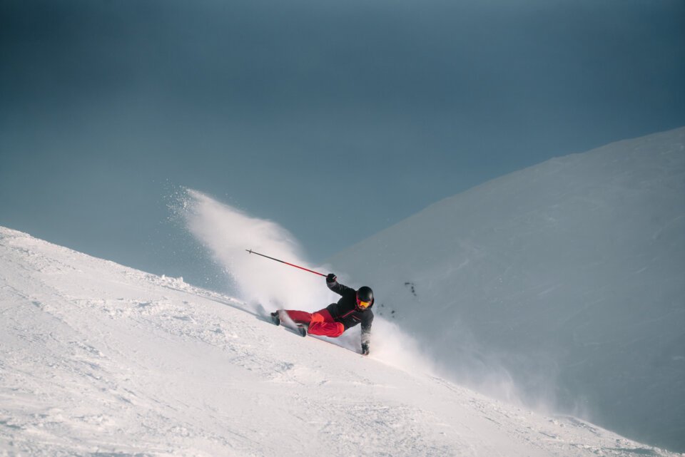 INTERSPORT Rent Atomic Skiing Perfect Ski Day Carving Skier carving down a snowy slope.